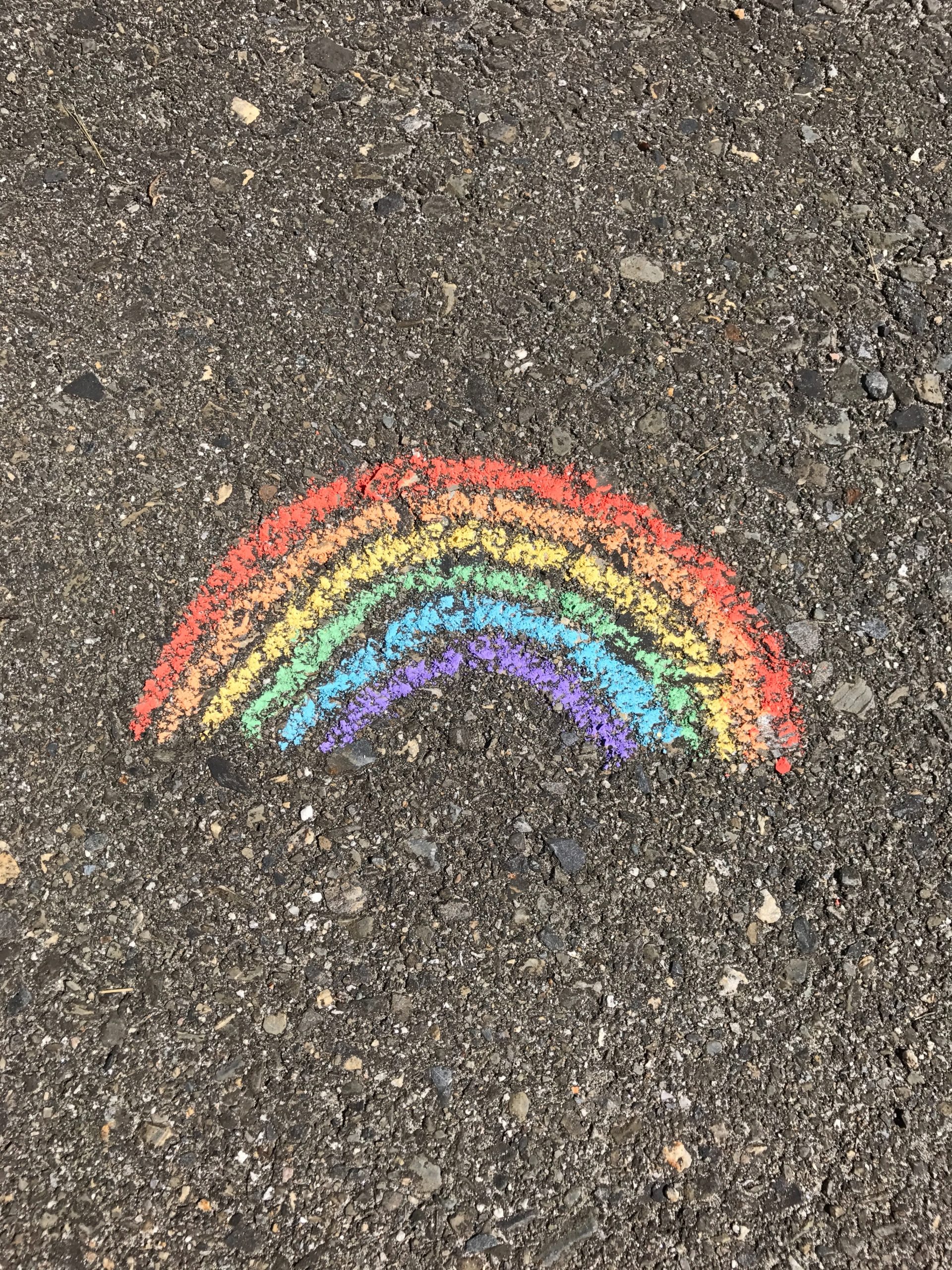 Ein Regenbogen, der mit bunter Kreide auf Asphalt gemalt wurde